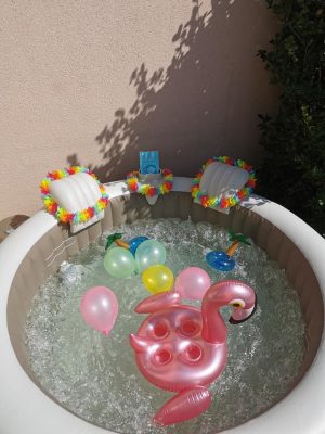 Spa gonflable décoré avec ballons, flamant rose et guirlandes hawaïennes en extérieur.