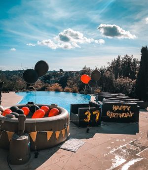 Spa gonflable décoré en noir et rouge avec ballons et guirlandes près d’une piscine à débordement