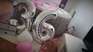Spa gonflable décoré avec ballons argentés “36”, pétales et ballons roses pour un anniversaire en intérieur.