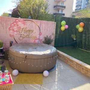 Spa gonflable installé sur une terrasse décorée avec fond “Happy Birthday” et ballons colorés.