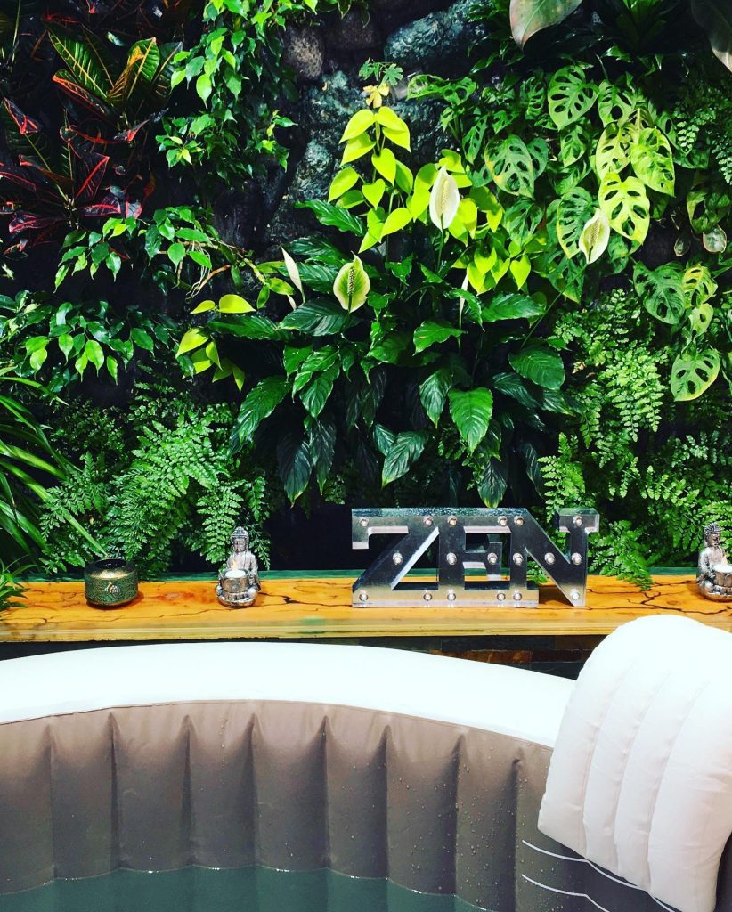 Spa gonflable décoré avec mur végétal et statues bouddha pour ambiance zen