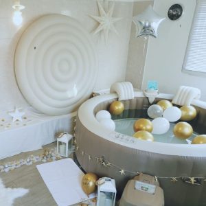 Spa gonflable décoré en blanc et or avec ballons, étoiles et lanternes dans une pièce lumineuse.