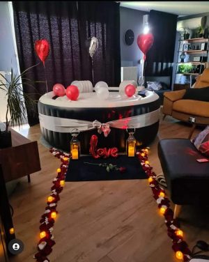 Installation romantique Dans Ma Bulle avec spa gonflable décoré, pétales de roses, lanternes et ballons cœur.