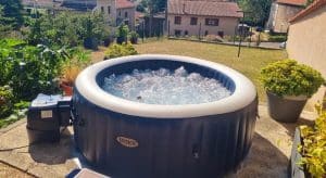 Spa gonflable installé dans un jardin surélevé avec vue sur un village et des collines.