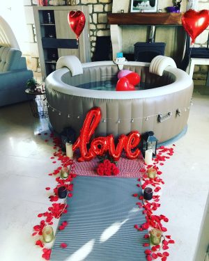 Spa orné d’un ballon “love”, pétales rouges et lanternes décoratives.