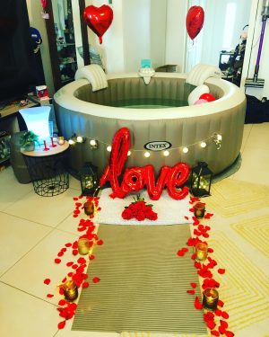 Spa avec ballons, guirlande lumineuse et pétales rouges au sol.